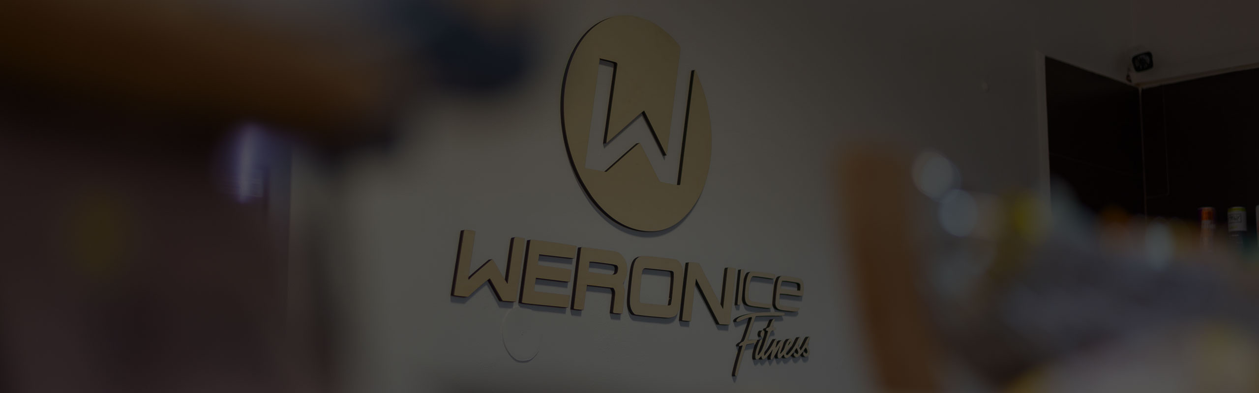 Logo Weronice Fitness z dreva na bielej stene